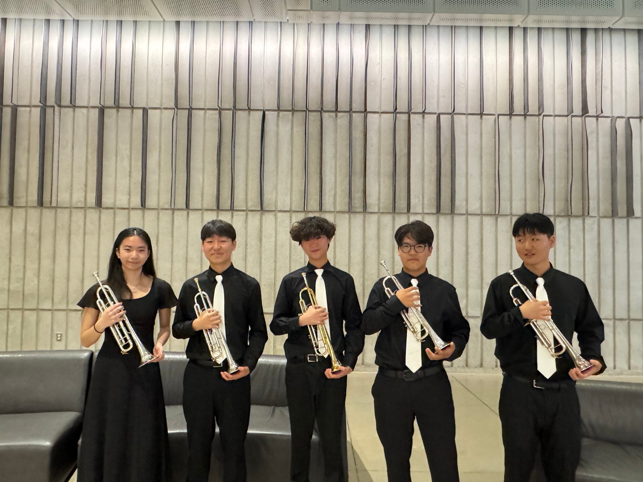 Five students in concert attire holding trumpets