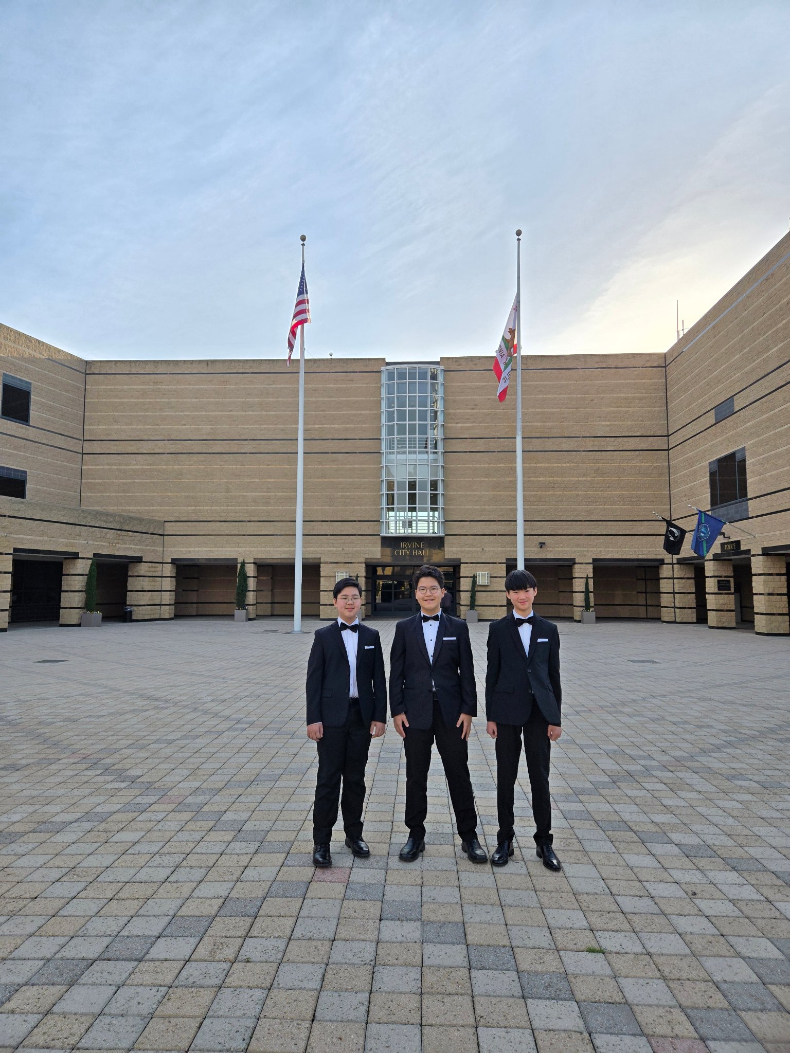 Three students in tuxedos standing in front of Irvine City Hall