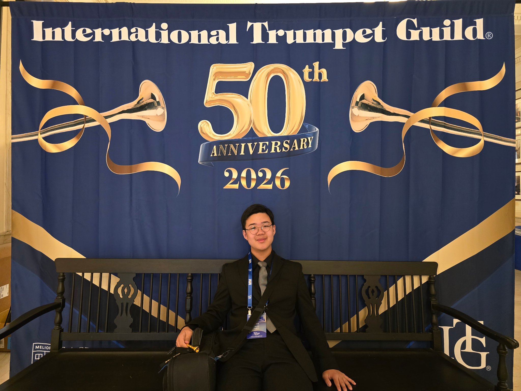 Student seated in front of International Trumpet Guild 50th Anniversary 2026 banner at Eastman