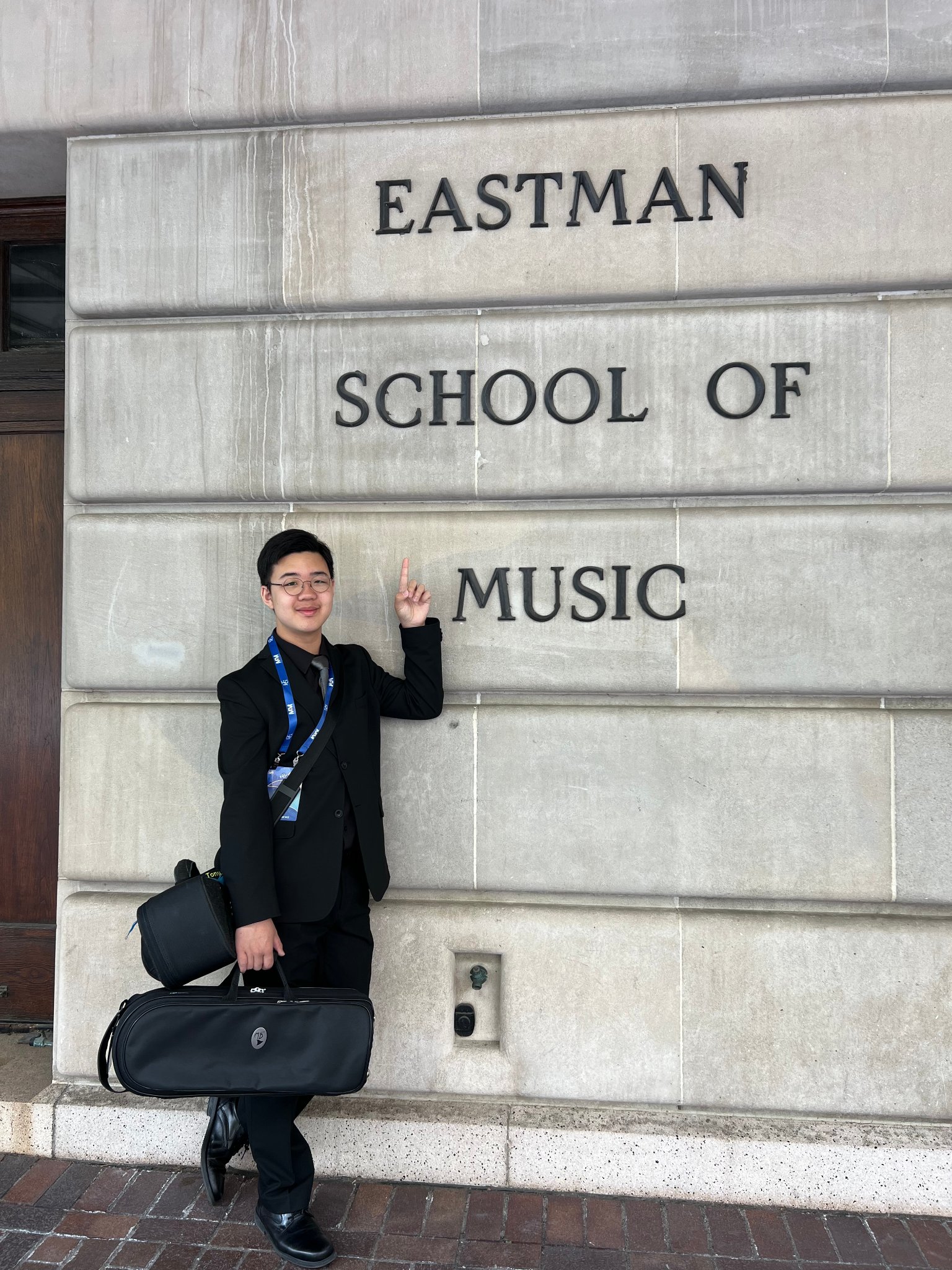 Student standing in front of Eastman School of Music sign with trumpet case
